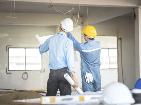 Hai kỹ sư xây dựng đang thảo luận bản thiết kế tại công trường.