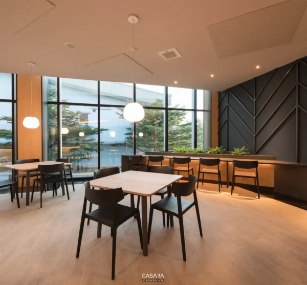 Không gian quán cafe hiện đại với cửa kính lớn nhìn ra cây xanh.