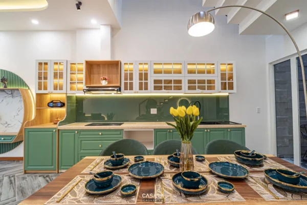 Phòng bếp hiện đại với tủ bếp xanh, bàn ăn gỗ sáng.