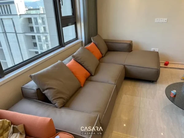 Phòng khách hiện đại với bộ sofa góc màu xám và gối cam.