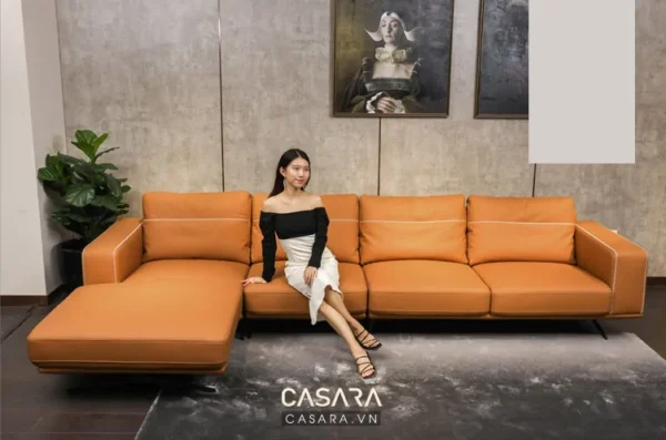 Cô gái trẻ ngồi trên bộ sofa da màu cam hiện đại, sang trọng.