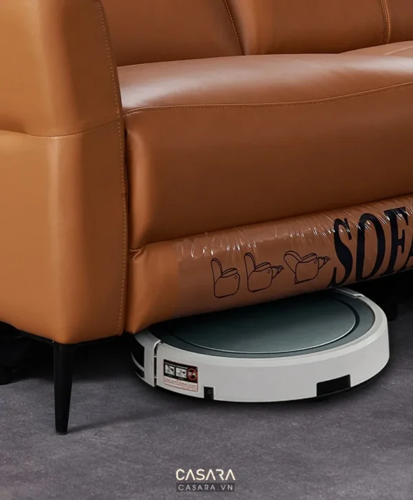 Robot hút bụi làm sạch dưới ghế sofa da màu nâu hiện đại.