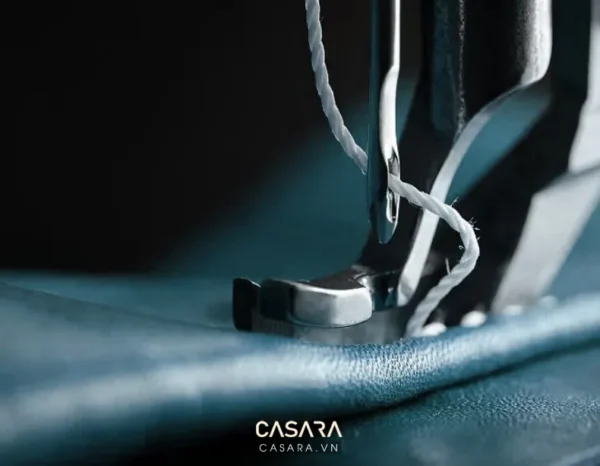 Chiếc máy may đang hoạt động trên nền vải xanh đậm.