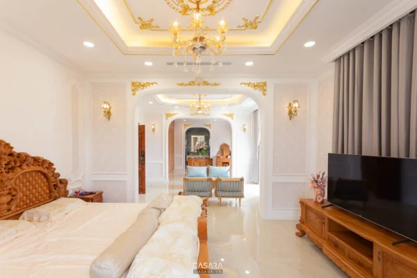 Phòng ngủ xa hoa với nội thất gỗ chạm khắc tinh xảo và đèn chùm lộng lẫy.