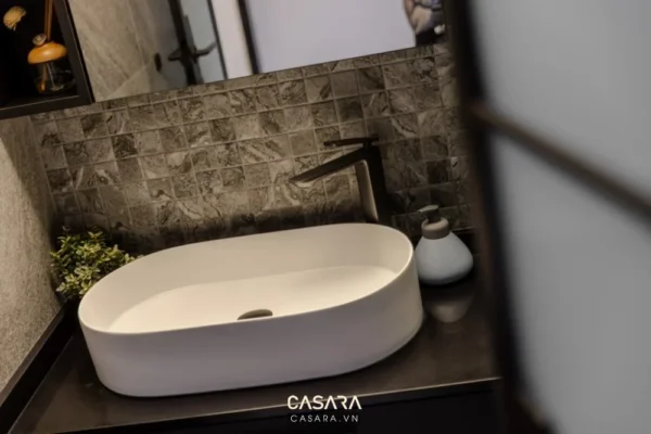 Phòng tắm hiện đại với bồn rửa trắng và tường ốp đá xám.