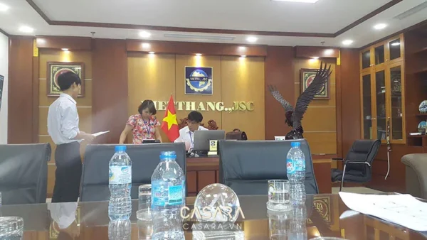 Phòng họp trang trọng với bàn dài, cờ và logo công ty.