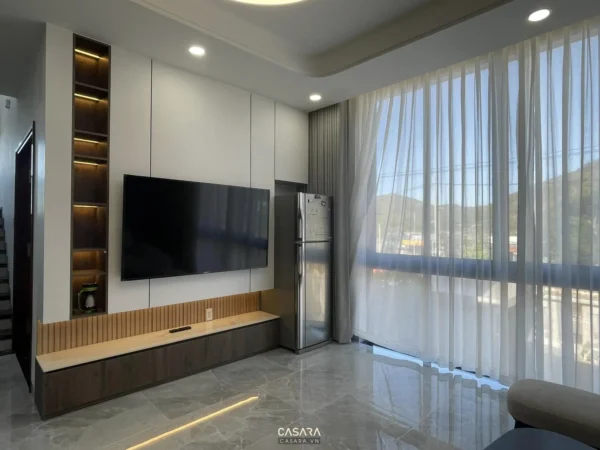 Phòng khách hiện đại, sang trọng với TV lớn và cửa sổ thoáng đãng.