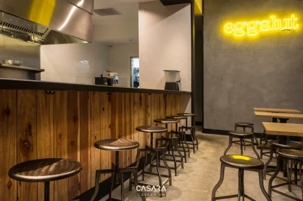 Không gian quán ăn Eggslut hiện đại với quầy bar gỗ và đèn neon.