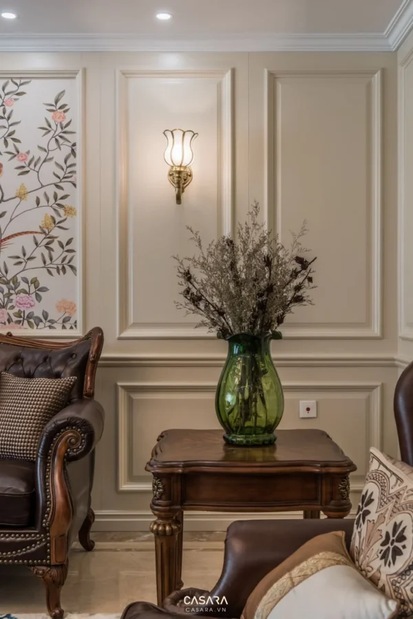 Phòng khách trang nhã với bình hoa và đèn tường cổ điển.