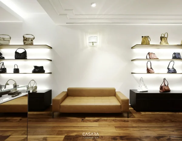 Cửa hàng thời trang sáng trọng với kệ túi xách và sofa màu be.