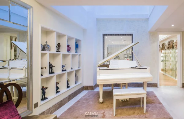 Phòng khách sang trọng với đàn piano trắng và kệ sách trang trí.