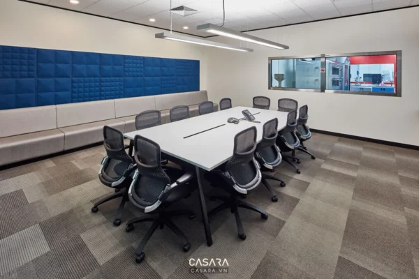 Phòng họp hiện đại với bàn trắng dài, ghế xoay và tường cách âm.