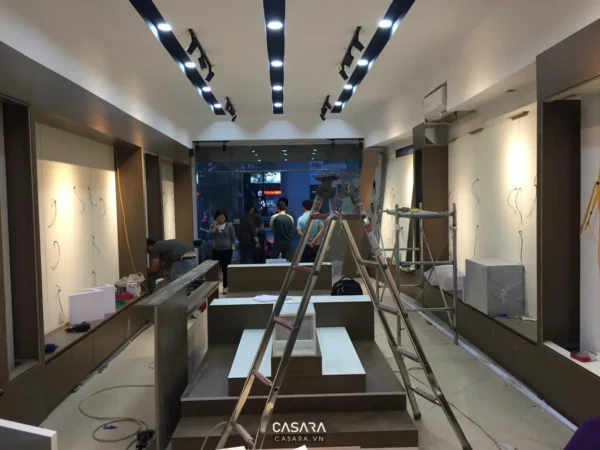Hiện trường thi công showroom có thang, trần đèn, tủ kệ và đội lắp đặt nội thất