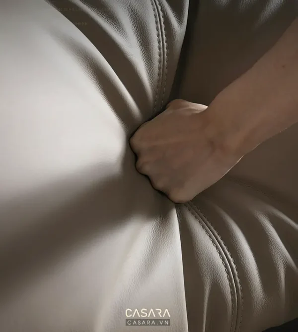 Bàn tay nắm chặt mép ghế sofa da màu be êm ái, tạo cảm giác thư giãn.