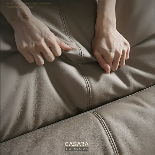 Bàn tay người đang chạm vào bề mặt sofa da màu be nhạt.