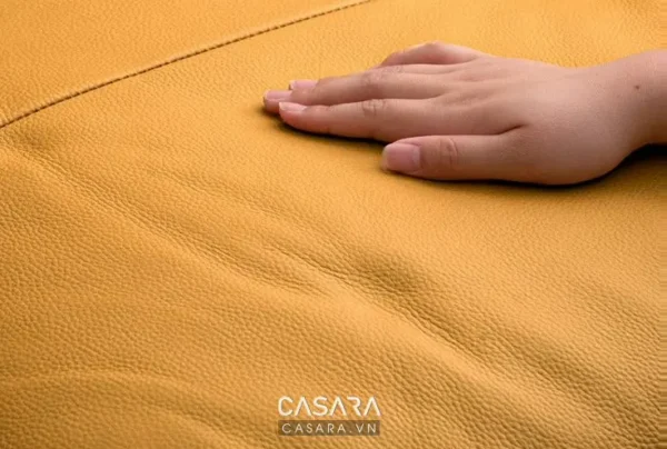 Bề mặt da màu vàng nhạt, mịn màng, được sờ chạm bởi bàn tay.