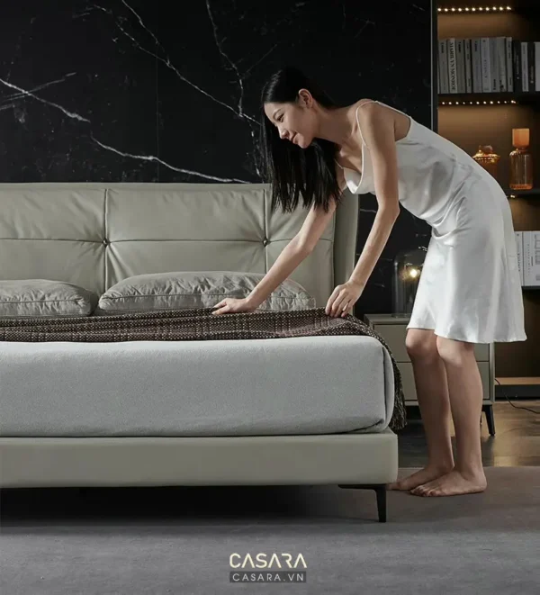 Người phụ nữ chỉnh chăn ga gối đệm trong phòng ngủ sang trọng.