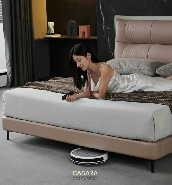 Người phụ nữ thư giãn trên giường, robot hút bụi đang làm việc.