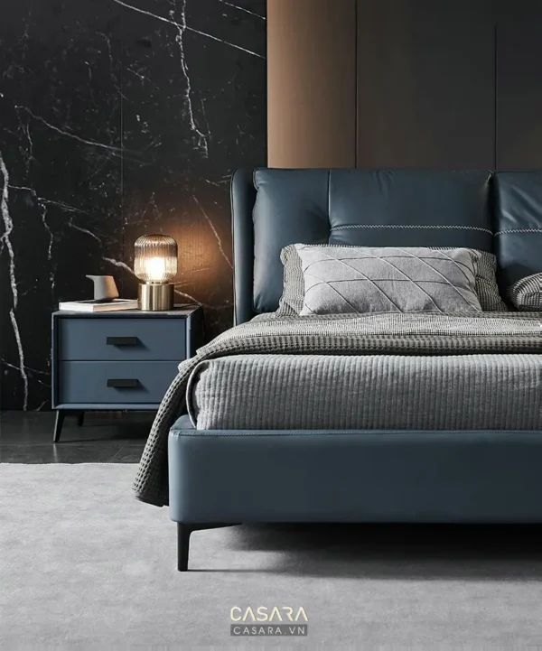 Phòng ngủ hiện đại, sang trọng với giường màu xanh đậm và đèn bàn vàng.