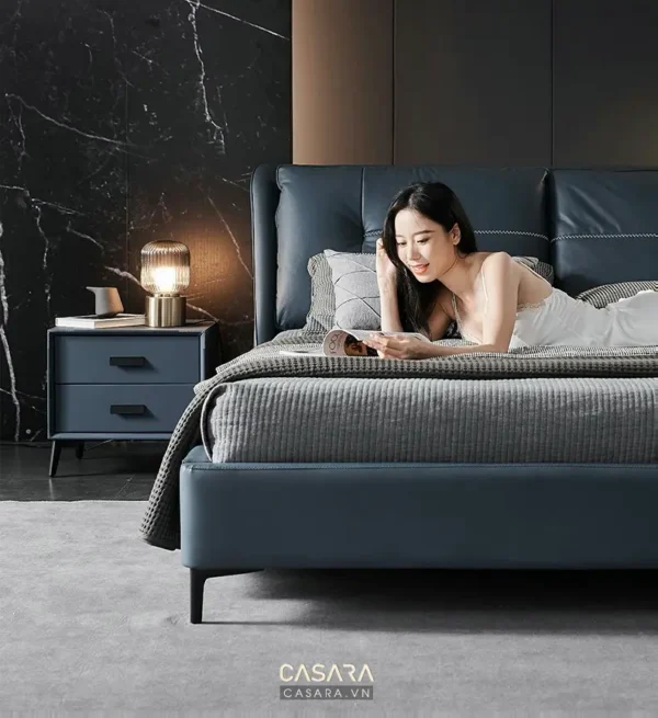 Phòng ngủ sang trọng với giường da xanh và cô gái đang đọc sách.