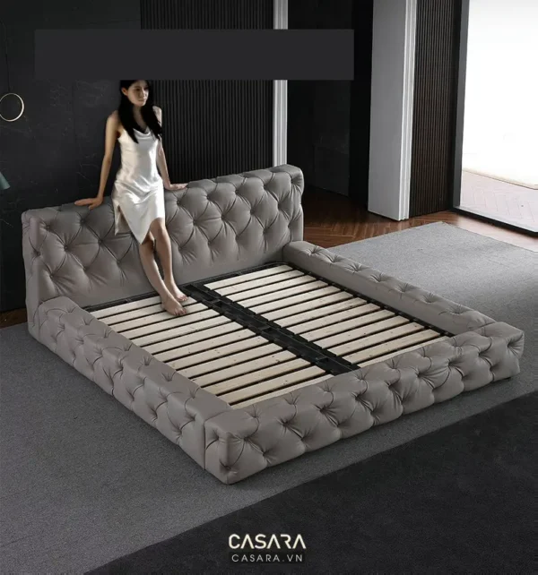 Nữ người mẫu tựa vào giường bọc vải nhung sang trọng, hiện đại.