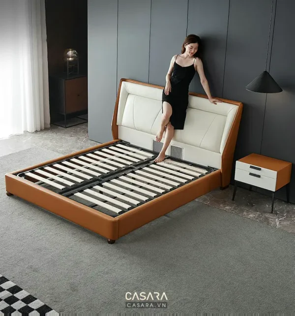 Người phụ nữ ngồi trên giường màu nâu nhạt, phòng ngủ hiện đại.