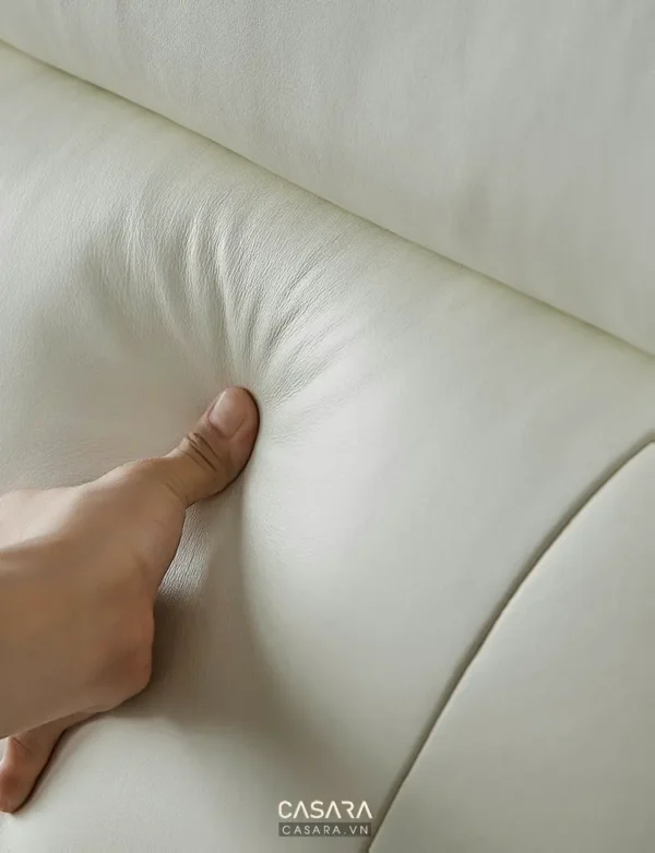 Bàn tay kiểm tra chất liệu da mềm mại của ghế sofa trắng.