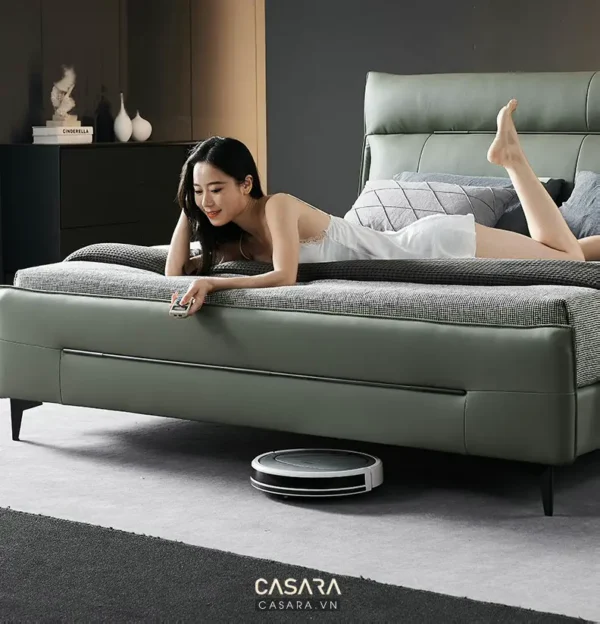 Cô gái thư giãn trên giường, robot hút bụi đang làm việc.