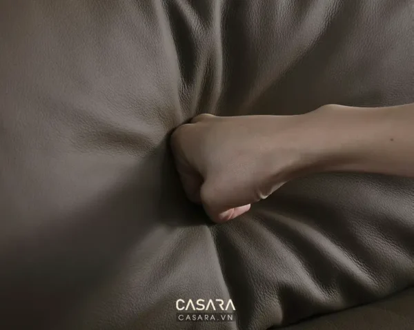 Bàn tay nắm chặt lớp đệm sofa mềm mại màu nâu sẫm.