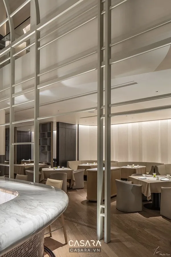 Nội thất luxury phong cách indochine phòng ăn với bàn ăn gỗ, ghế bọc nệm, đèn thả, vách trang trí mây hoặc gỗ và tông màu ấm