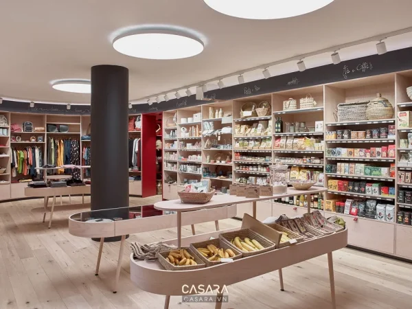 Không gian showroom bán lẻ sáng màu với kệ hàng, bàn trưng bày và hệ đèn trần