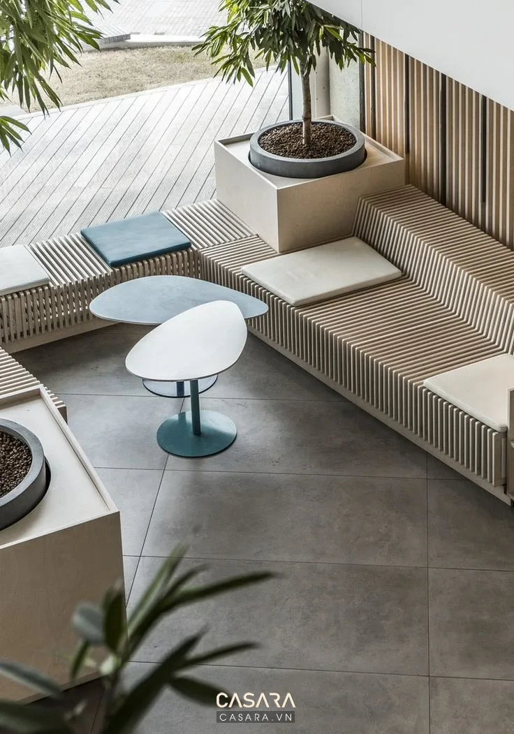 Ban công căn hộ chung cư có sofa chữ L, bàn tròn nhỏ, cây xanh và nền gạch sáng.