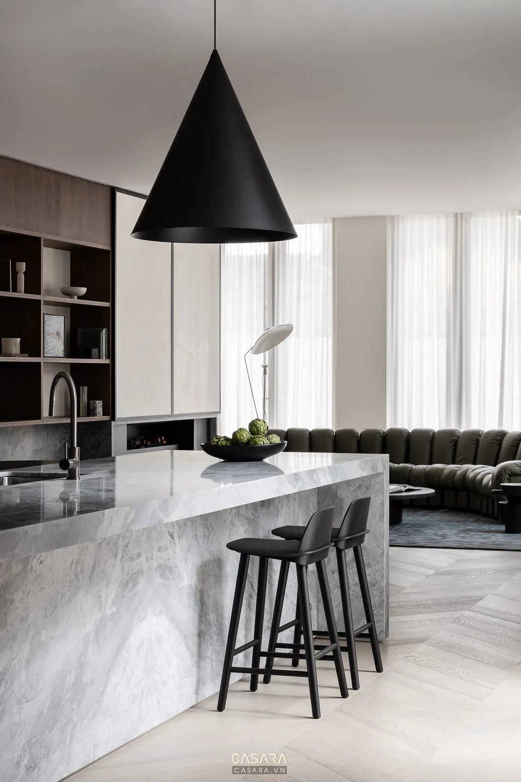 Đảo bếp đá xám kết hợp quầy bar trong căn hộ chung cư mở, nối khu bếp với phòng khách.