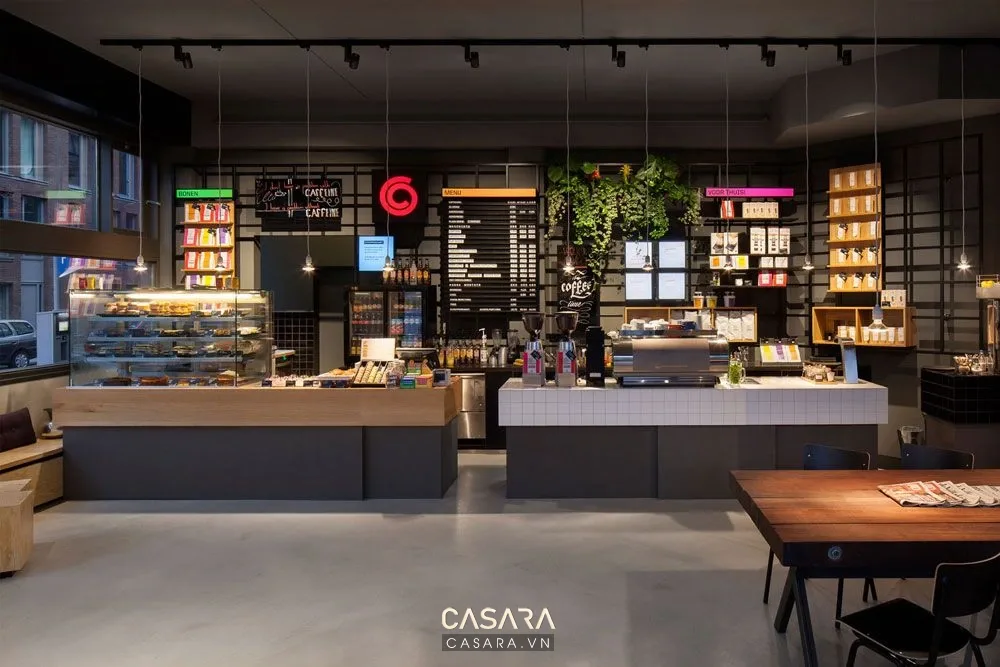 Quán cà phê nhỏ mặt tiền phố có quầy order cafe gần cửa, menu treo tường, bàn ghế gỗ nhỏ và khách mua cà phê mang đi