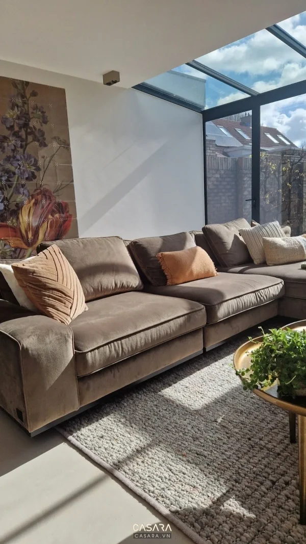 Sofa xám dài với bàn trà kính và kệ tường trang trí