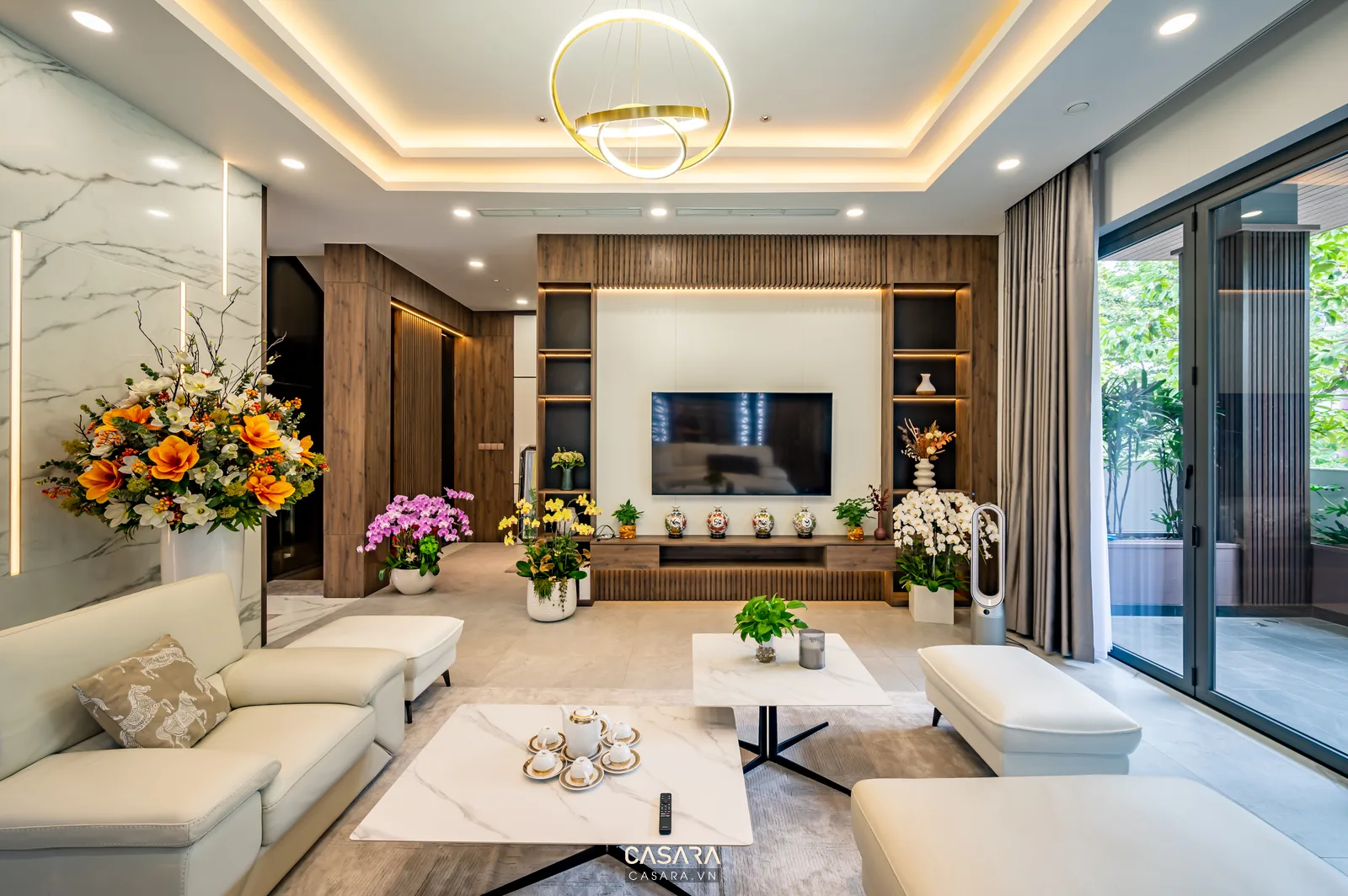 Phòng khách hiện đại có sofa sáng màu, vách tivi gỗ và cửa kính lớn
