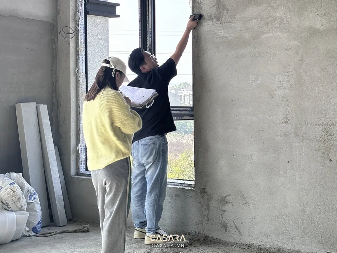 Hai người đang đo đạc và ghi chú tại khu vực cửa sổ trong công trình thô