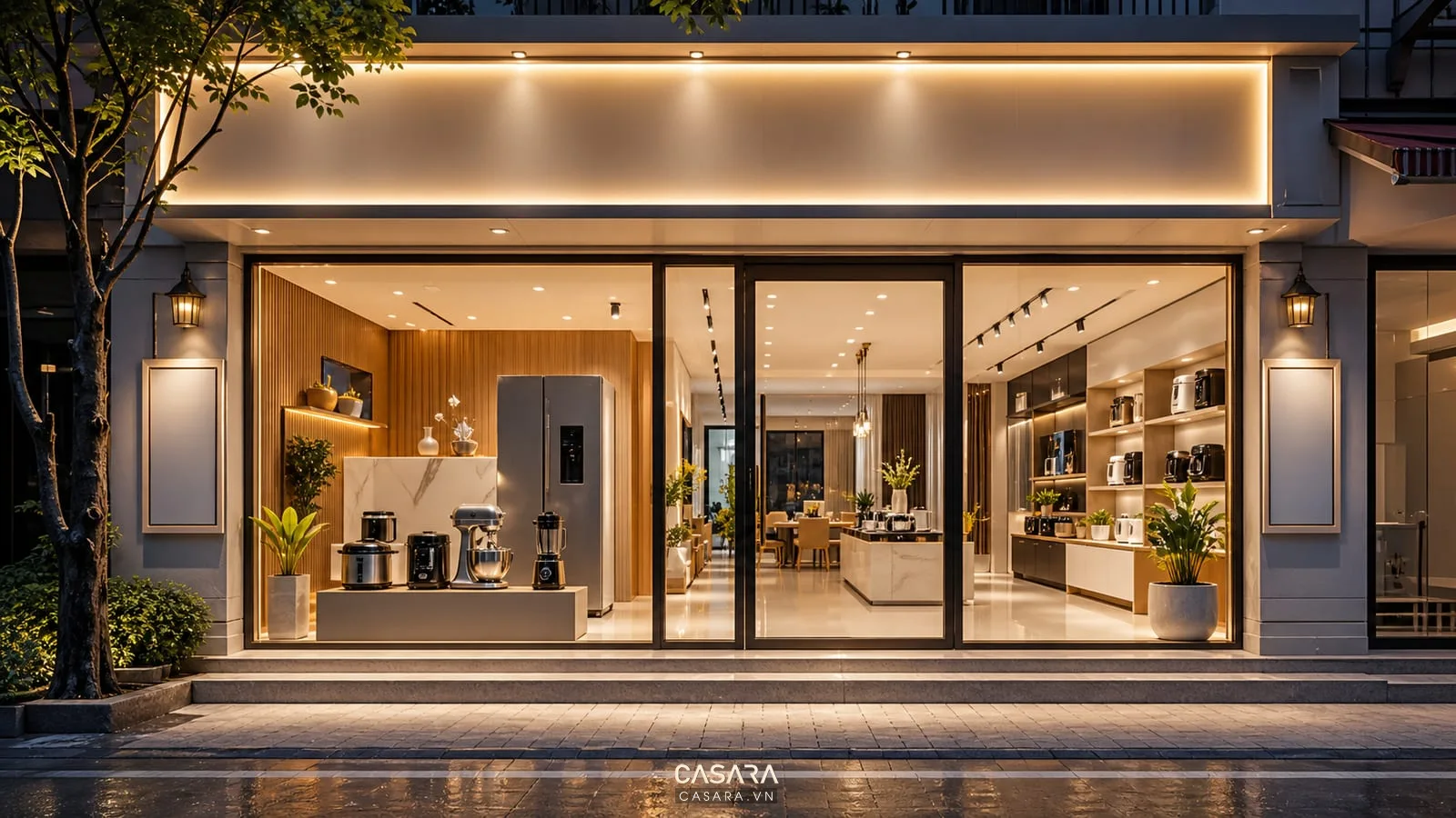 Mặt tiền showroom đồ gia dụng buổi tối có cửa kính sáng, bảng hiệu rõ, thiết bị bếp, tủ lạnh và trưng bày gọn không nhiều poster.