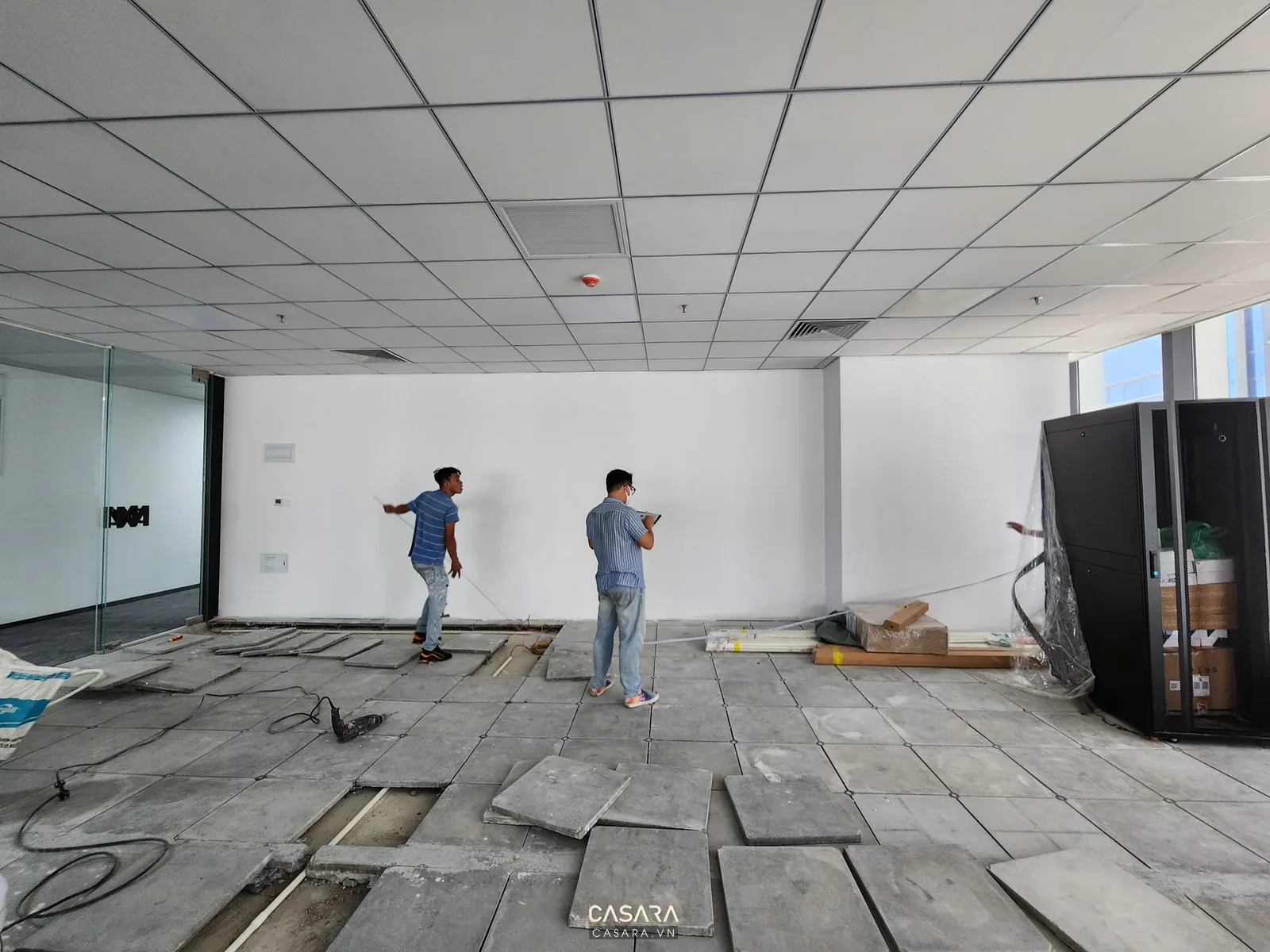Không gian văn phòng đang thi công với sàn nâng, trần thả và đội khảo sát hiện trạng