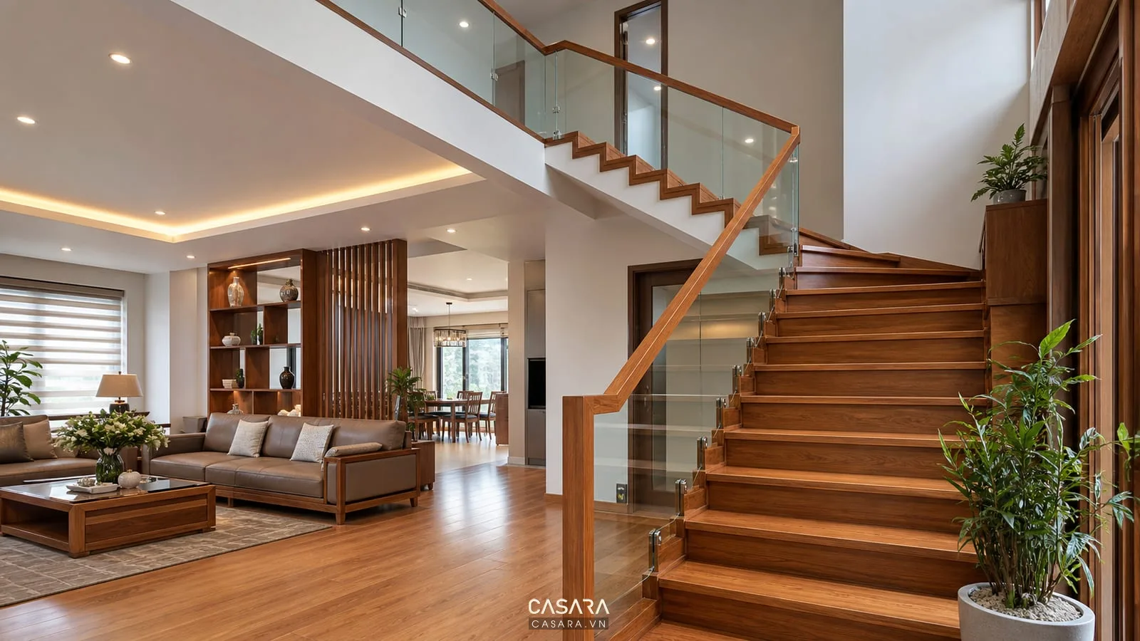 Cầu thang gỗ nhà 2 tầng với tay vịn gỗ, lan can kính, tường sáng, đèn hắt ấm và phòng khách thanh lịch