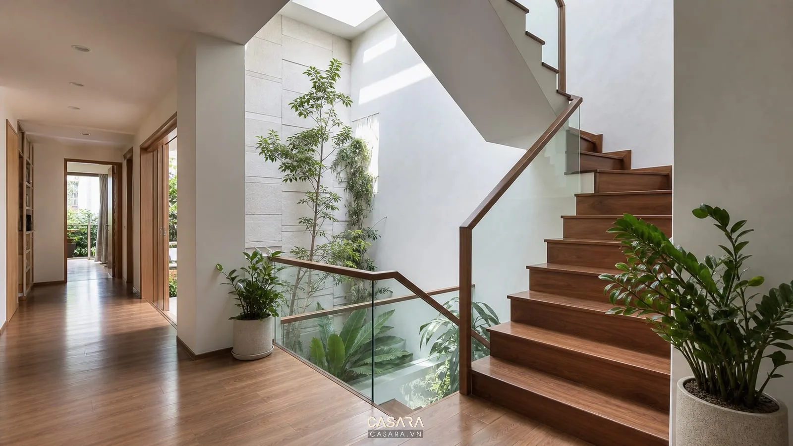 Cầu thang chữ L nhà ống cạnh giếng trời với lan can kính và cây xanh