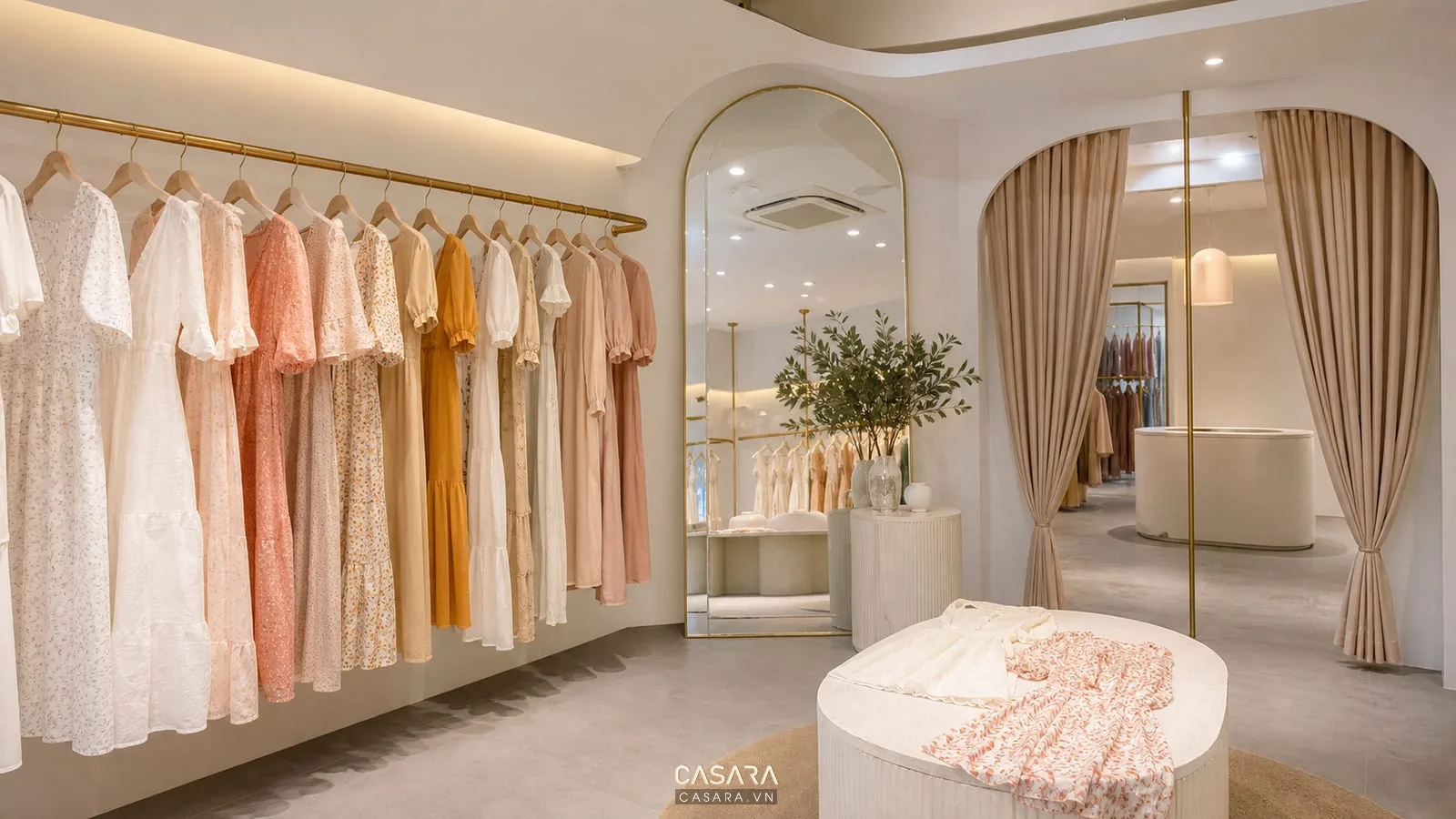 Hình ảnh shop quần áo nữ đẹp phong cách boutique với váy treo trên thanh kim loại, gương lớn, rèm mềm và đèn trang trí ánh sáng ấm