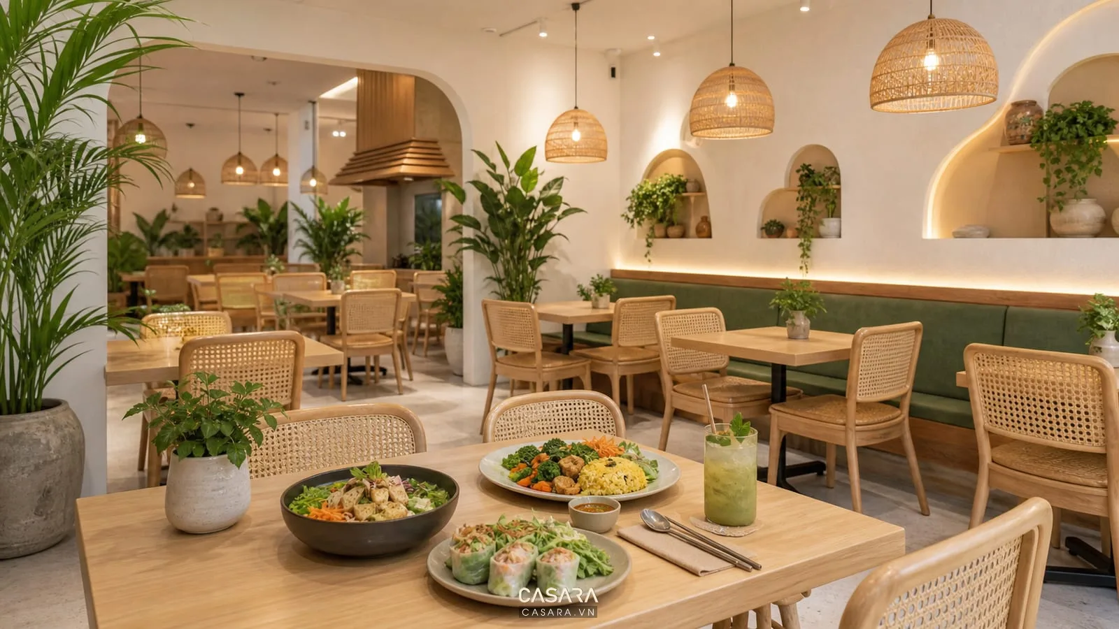 Nhà hàng chay với bàn gỗ sáng, ghế mây, cây xanh, tường trắng ấm, đèn thả nhẹ và món ăn chay trên bàn.