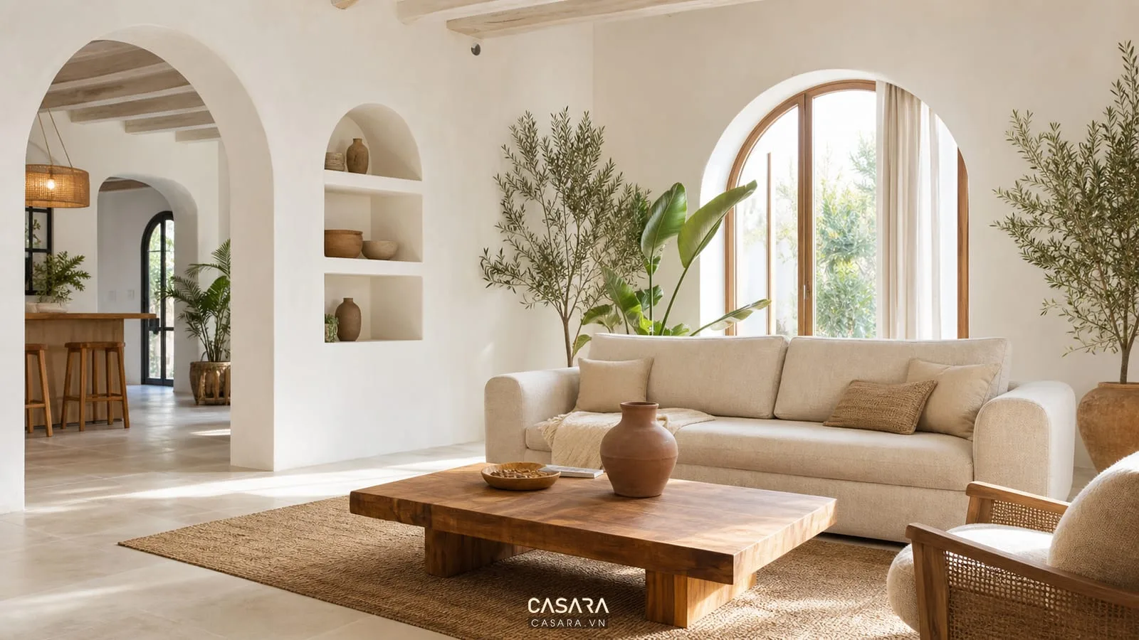 Nhà địa trung hải phòng khách có tường trắng kem, cửa vòm lớn, sofa vải be, bàn gỗ, thảm dệt, cây xanh và ánh sáng ban ngày