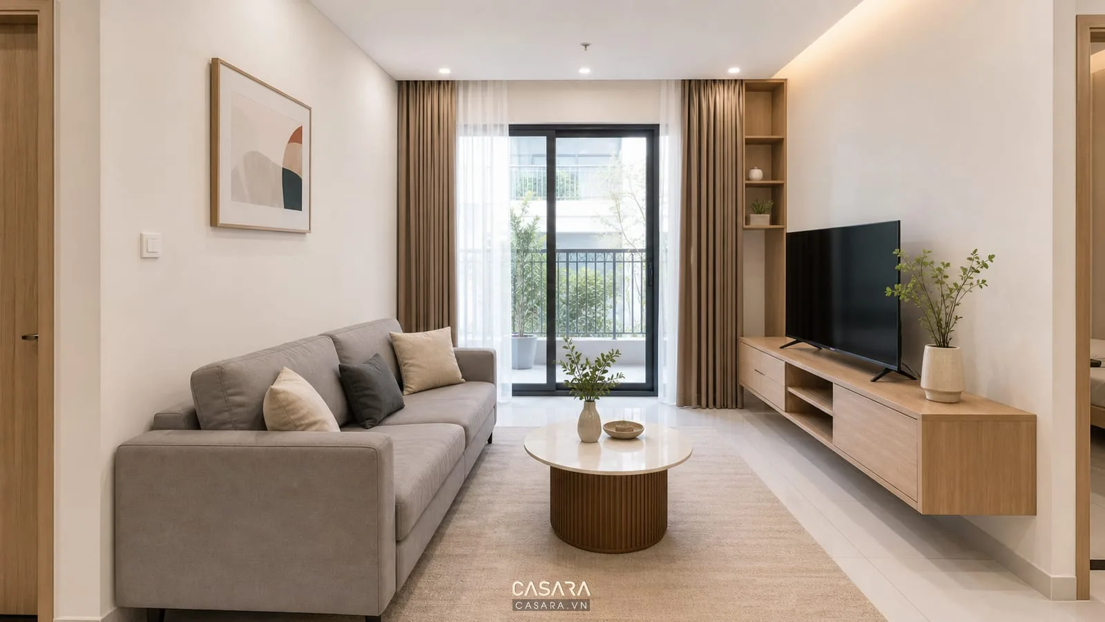 Phòng khách chung cư nhỏ có mặt bằng mở với sofa chữ I màu xám nhạt, bàn trà tròn, kệ tivi treo tường, bếp và bàn ăn phía sau gọn gàng