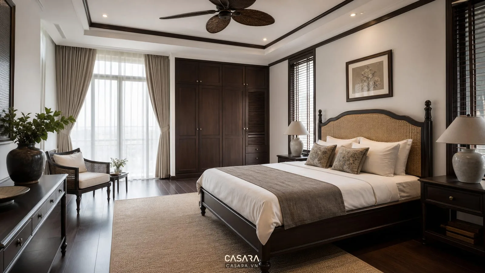 Phòng ngủ phong cách nội thất đông dương với giường ngủ gỗ, đầu giường mây đan, tủ áo cánh phẳng, quạt trần, sàn gỗ và rèm vải sáng