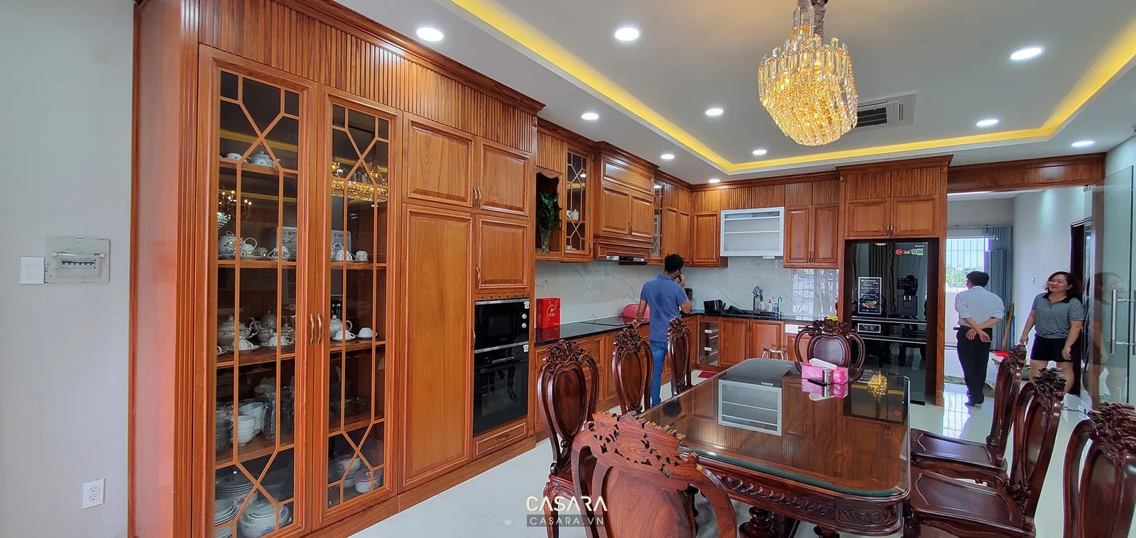 Phòng bếp rộng với hệ tủ gỗ, bàn ăn lớn và đèn chùm trang trí