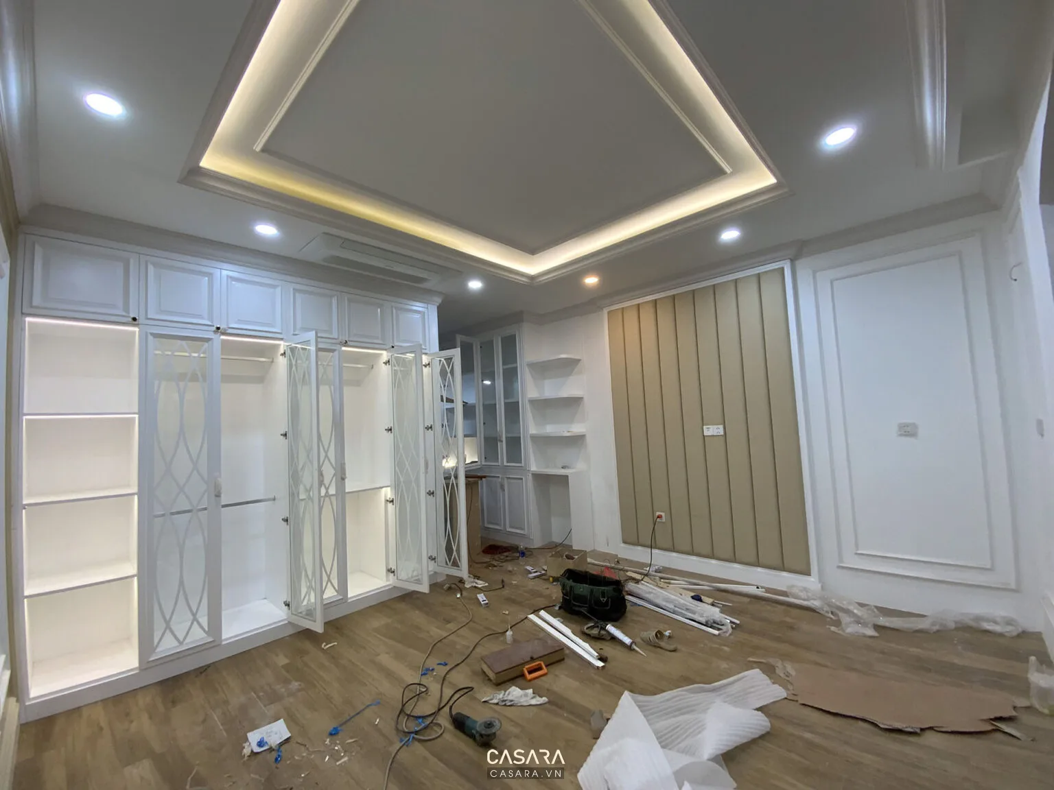 Phòng ngủ đang thi công với tủ áo trắng, trần giật cấp và hệ đèn âm trần