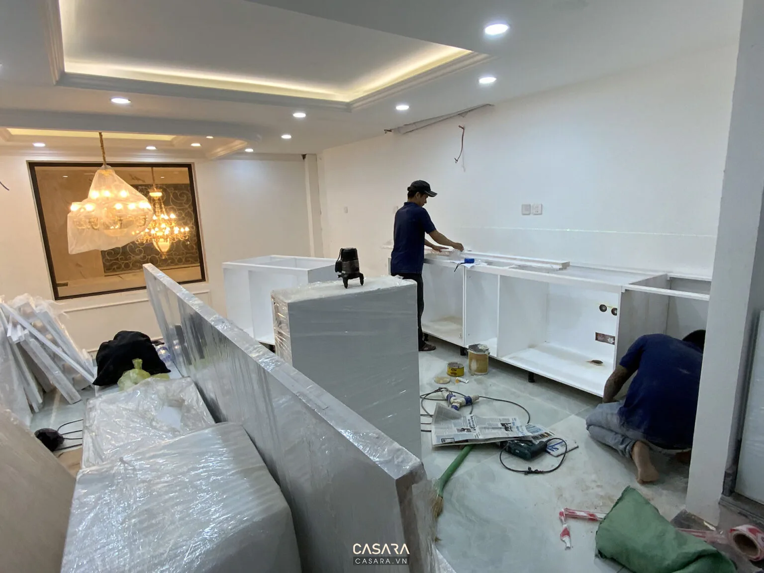 Thợ đang lắp đặt tủ bếp trắng trong không gian nhà ở đang hoàn thiện