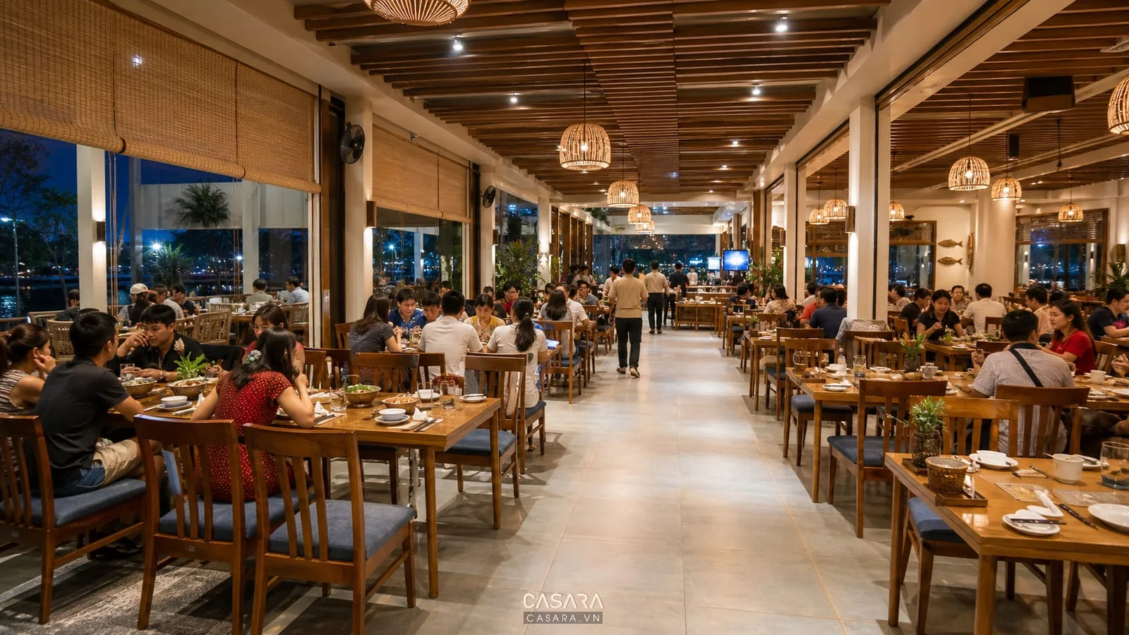 Khu bàn ăn nhà hàng hải sản có bàn ghép linh hoạt, ghế bọc nệm, lối đi rộng và ánh sáng ấm.